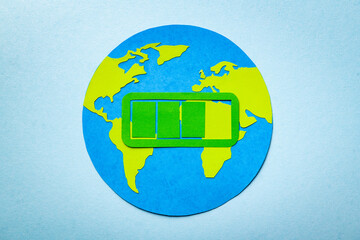 Paper cut concept of planet Earth on the blue background with the charging sign above. Green symbol of energy almost full.