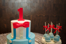 Festive Candy Bar For One Year Old Boy Birthday Party. Cake With Red Number 1 And Butterfly Bow On Shirt. Blue Cakepops With Red Bows.