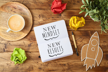 new mindset and new results text on notebook on wooden table with coffee cup and paper rocket. busin