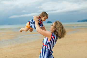 Grandmother and granddaughter playing on beach fun games looking smiling outdoors. Family bonding together on summer holiday travel activities recreation lifestyle. Travel with toddler