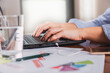 © René Stevens - Close-up of a businesswoman's hands using a laptop in the office, with a glass of water.