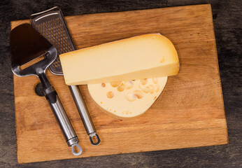 Two types cheese, cheese slicer and grater on cutting board