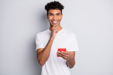 Sticker - Portrait of brunet optimistic cool curly guy hold telephone hand chin wear white t-shirt isolated on grey background