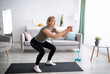 © Prostock-studio - Positive senior lady doing squats on domestic workout in living room, free space