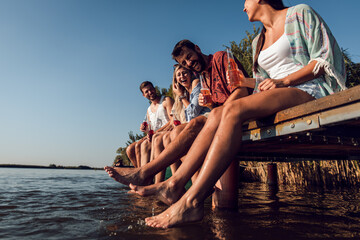 Wall Mural - Group of friends sitting on the edge of a pier having fun and enjoying a summer day at the lake.