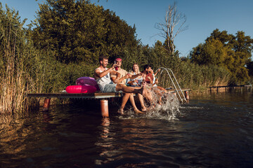 Wall Mural - Group of friends sitting on the edge of a pier having fun and enjoying a summer day at the lake.