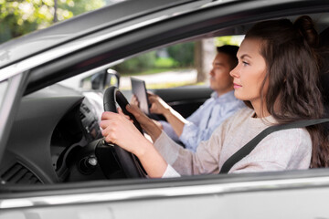 Wall Mural - driver courses and people concept - car driving school instructor teaching young woman to drive