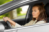 Fototapeta  - safety and people concept - young woman or female driver driving car in city