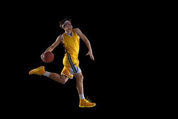 Wall Mural - Young Caucasian basketball player training isolated on black background.