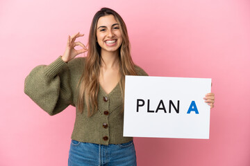 Wall Mural - Young caucasian woman isolated on pink background holding a placard with the message PLAN A with ok sign