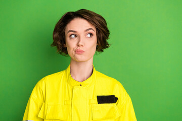 Poster - Photo of young woman firefighter hesitate doubt think look empty space isolated over green color background