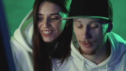 Portrait of modern man and woman using a computer on a neon light colorful background. Close-up.