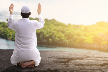 Rear view of Asian Muslim man sitting while raised hands and praying