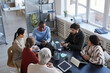 © Seventyfour - High angle view at diverse group of business people at table during briefing meeting in office, focus on smiling African-American man