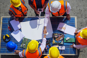 Wall Mural - Holding hands top view of Architectural engineers working on solar panel and his blueprints with Solar photovoltaic equipment on construction site. meeting, discussing, designing