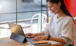 © sarawutnirothon - A young woman is operating a laptop in a cafe with a smiling expression.