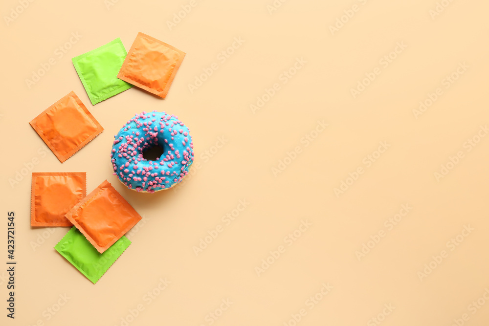 Sweet donut and condoms on color background. Erotic concept - obrazy, fototapety, plakaty 