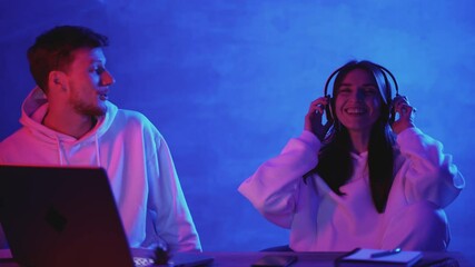 Modern man and woman using a computer and wireless headphones on a neon light colorful background