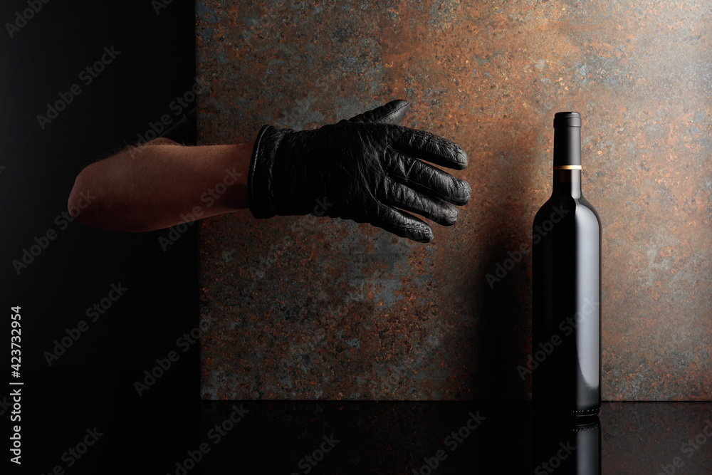 Hand in  glove reaches for a bottle of red wine. - obrazy, fototapety, plakaty 