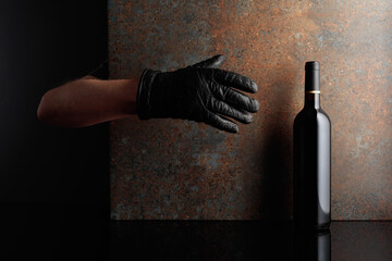 Hand in  glove reaches for a bottle of red wine.