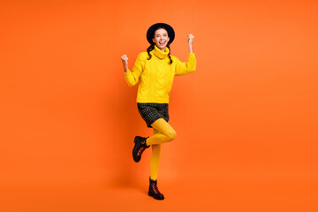 Wall Mural - Full size photo of optimistic girl hands fists wear yellow sweater cap skirt shoes isolated on orange background