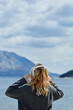 Back view of blonde woman wearing headphones listening positive music podcast from smartphone application against the sea