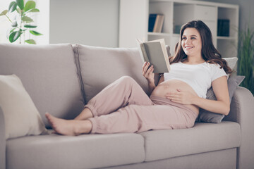 Wall Mural - Full size photo of attractive young woman mom hold read book lie couch touch belly indoors inside house