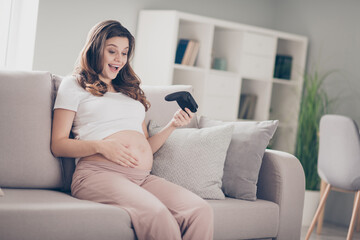 Sticker - Photo of excited happy mother baby kick touch belly hold joystick gamer sit sofa inside living room indoors