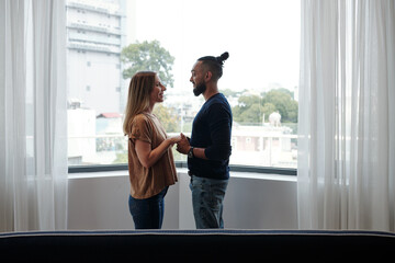 happy mixed-race couple in love standing on balcony, holding hands and looking at each other