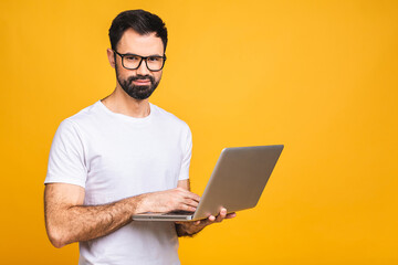 Wall Mural - Confident business expert. Confident young handsome bearded man in casual holding laptop and smiling while standing over isolated yellow background.