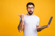 © denis_vermenko - Confident business expert. Confident young handsome bearded man in casual holding laptop and shocked amazed while standing over isolated yellow background. Pointing finger.