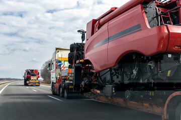 Wall Mural - Many heavy industrial truck with semi trailer platform transport disassembled combine harvester machine on common highway road on sunset or sunrise day. Agricultural equipment transportation service