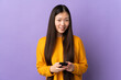 © luismolinero - Young Chinese girl over isolated purple background sending a message with the mobile