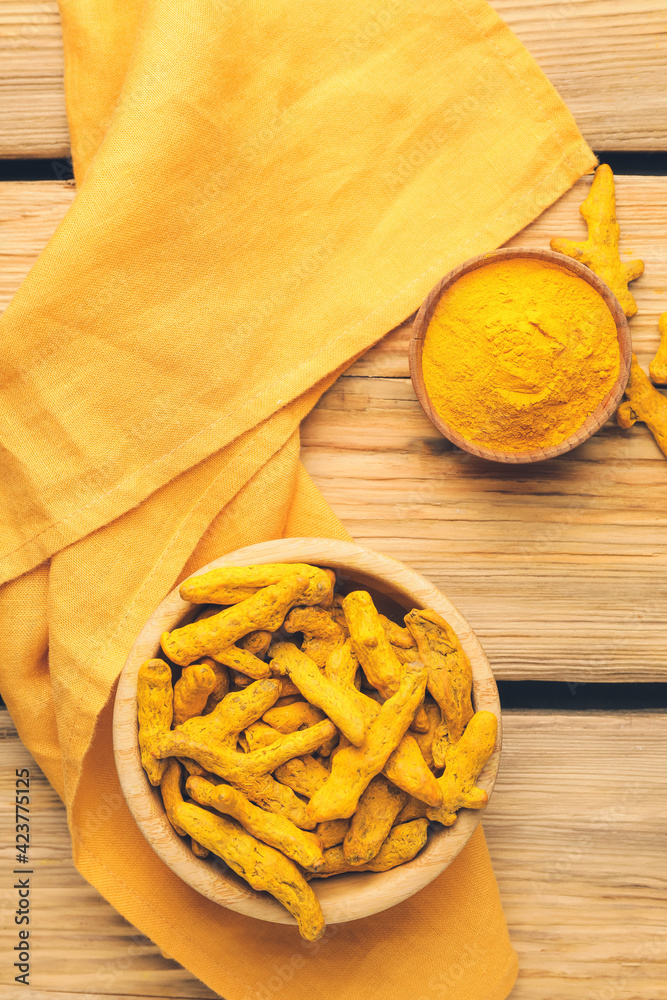 Bowls with turmeric powder and roots on wooden background