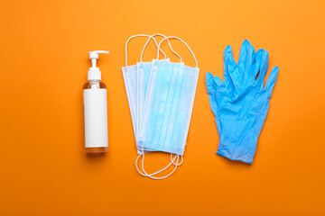 Medical masks, antiseptic and protective gloves on color background