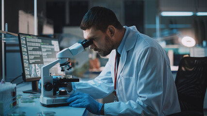  Medical Research Scientist Conducts DNA Experiments Under Digital Microscope in a Biological Applied Science Laboratory. Handsome Caucasian Lab Engineer in White Coat Working on Vaccine and Medicine.