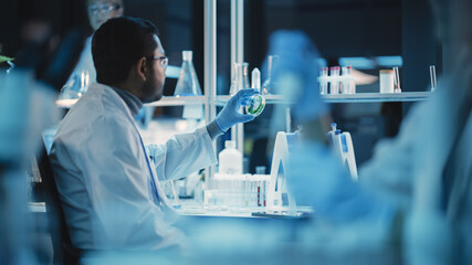 Wall Mural - Shot of an Indian Male Working on DNA, Analyzing Green Samples in a Petri Dish. He is Using Microscope and Working in a Modern Applied Science Laboratory. Dark Lab with Cold Color Grading.