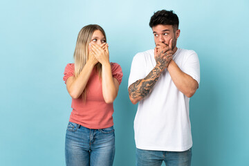 Young caucasian couple isolated on blue background covering mouth with hands