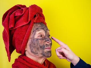 An old, elderly woman is doing facial treatments. Yellow background. The pensioner made a mask with vitamins for lifting and rejuvenation from deep clay. Facial care in old age. Personal hygiene, beau