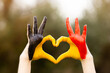 Kid hands painted in Belgium flag color show symbol of heart and love gesture on nature background