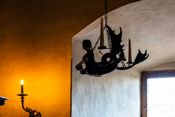 Silhouette of vintage candelabrum depicting mermaid with two unfired candles, and one burning candle on the wall.