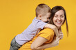 © ViDi Studio - Happy young woman have fun with cute child baby boy 5-6-7 years old in violet t-shirt stand behind hug kiss Mommy little kid son together isolated on yellow background studio Mother's Day love family
