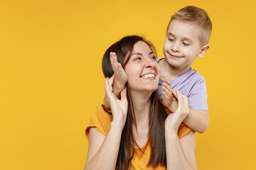 Wall Mural - Happy young woman have fun with child baby boy 5-6-7 years old in violet tshirt Mommy little kid son close eyes with hands play guess who isolated on yellow background studio Mother's Day love family