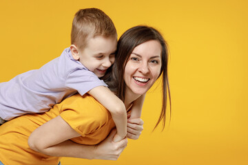 Wall Mural - Happy young woman have fun with cute child baby boy 5-6-7 years old in violet t-shirt stand behind hug kiss Mommy little kid son together isolated on yellow background studio Mother's Day love family