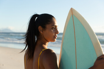 Wall Mural - Mixed race woman carrying surfboard on the beach