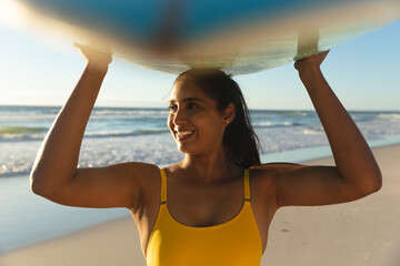 Wall Mural - Happy mixed race woman on the beach carrying surfboard on head