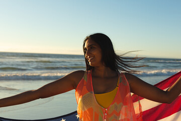 Wall Mural - Mixed race patriotic woman on the beach holding american flag