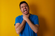 © Roquillo - young handsome caucasian man wearing blue t-shirt against yellow background shouting suffocate because painful strangle. Health problem. Asphyxiate and suicide concept.