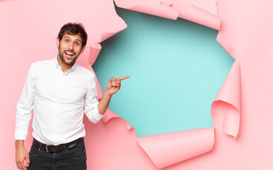 Wall Mural - young handsome indian man surprised expression against broken paper hole background