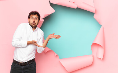 Wall Mural - young handsome indian man doubting or uncertain expression against broken paper hole background